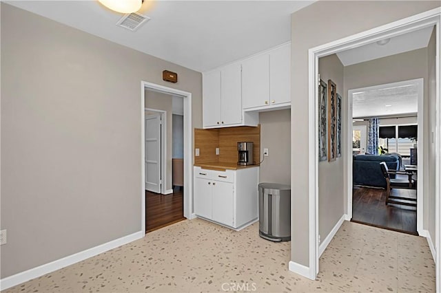 kitchen featuring baseboards, decorative backsplash, visible vents, and white cabinets