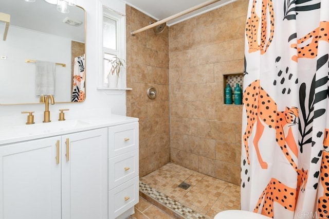 bathroom with visible vents, tiled shower, and vanity