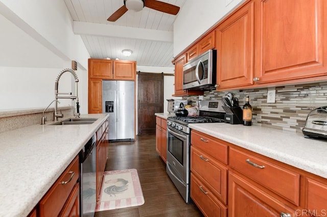 kitchen with a barn door, beamed ceiling, stainless steel appliances, light countertops, and a sink