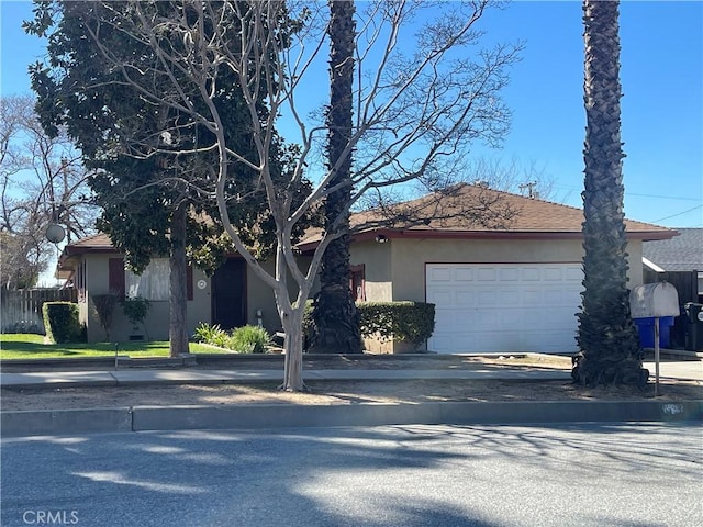 view of front facade featuring an attached garage, fence, concrete driveway, and stucco siding