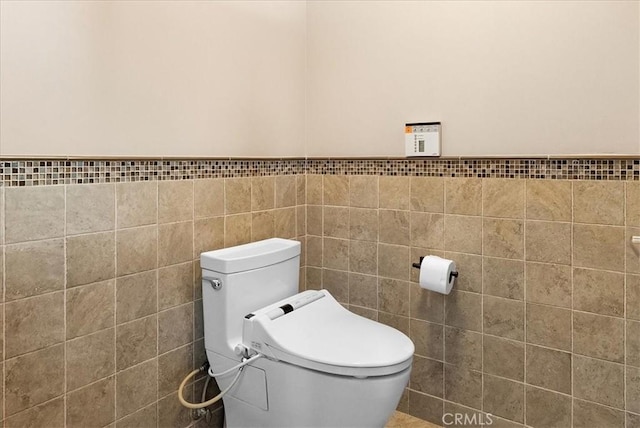 bathroom featuring toilet, wainscoting, and tile walls