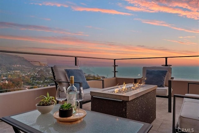 patio terrace at dusk with a water view, a balcony, and a fire pit