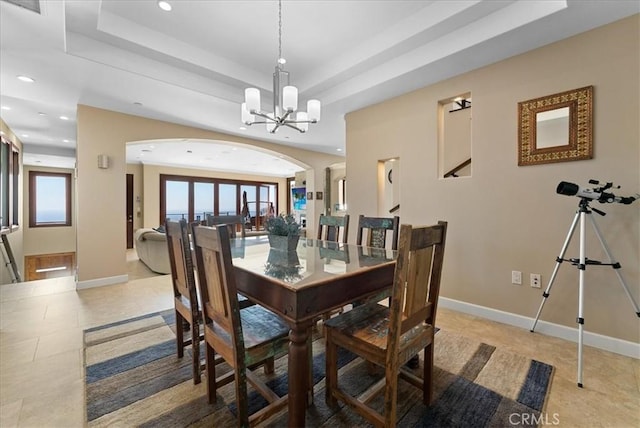 dining area featuring arched walkways, a raised ceiling, baseboards, and an inviting chandelier