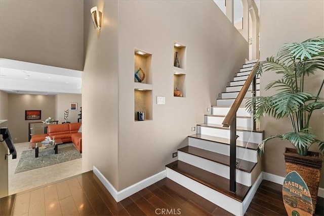 stairway featuring baseboards, a high ceiling, built in features, and wood finished floors