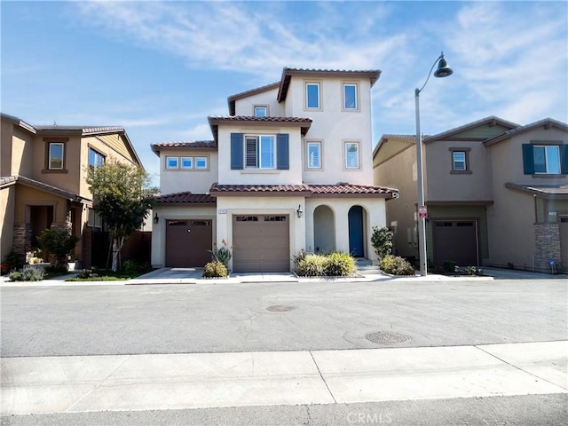 mediterranean / spanish-style home featuring a garage, driveway, a tiled roof, and stucco siding