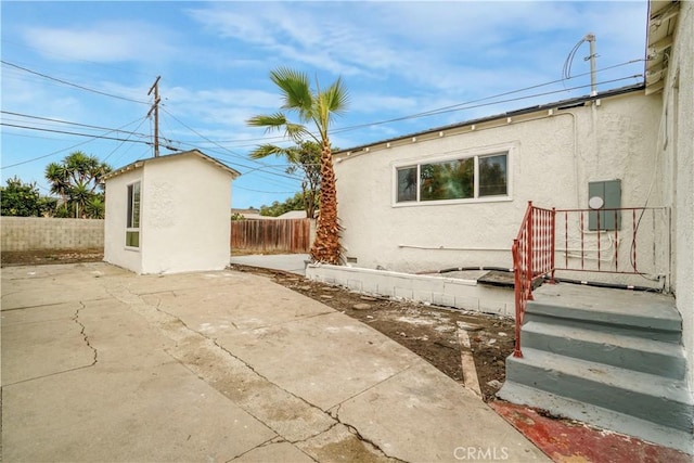 view of home's exterior featuring an outbuilding, a patio area, fence, and stucco siding