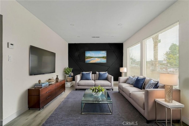 living room with light wood-type flooring, baseboards, an accent wall, and visible vents