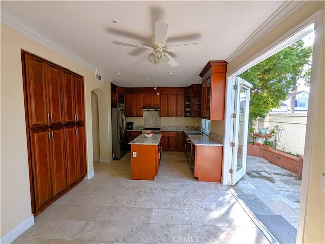 kitchen featuring under cabinet range hood, light countertops, appliances with stainless steel finishes, a center island, and glass insert cabinets