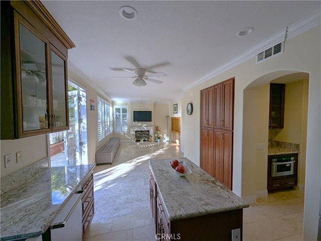 kitchen featuring a kitchen island, visible vents, stainless steel oven, ornamental molding, and glass insert cabinets