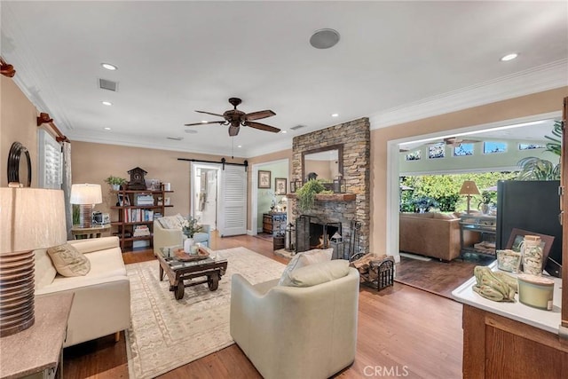 living room with a barn door, visible vents, light wood-style flooring, crown molding, and a stone fireplace