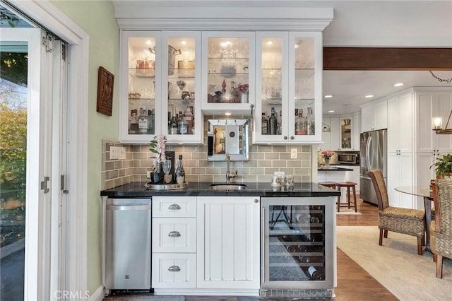 bar featuring beverage cooler, a sink, appliances with stainless steel finishes, backsplash, and wet bar