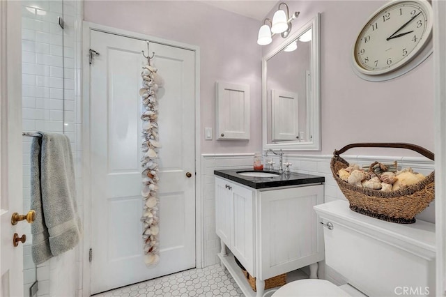 full bath with toilet, vanity, tile walls, wainscoting, and a tile shower