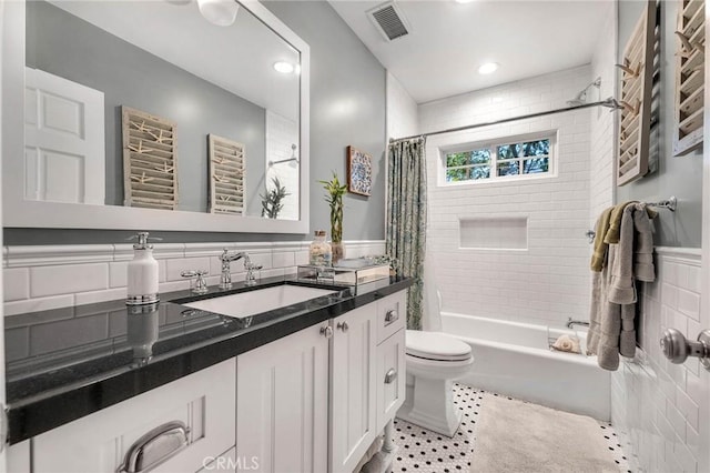 bathroom with toilet, a wainscoted wall, shower / bathtub combination with curtain, vanity, and tile walls