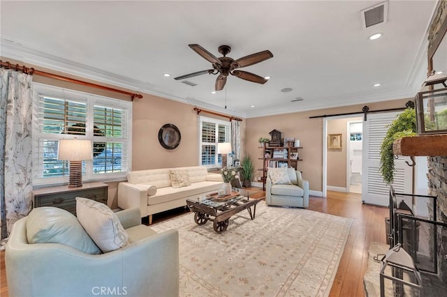 living room with light wood finished floors, a barn door, visible vents, ceiling fan, and ornamental molding