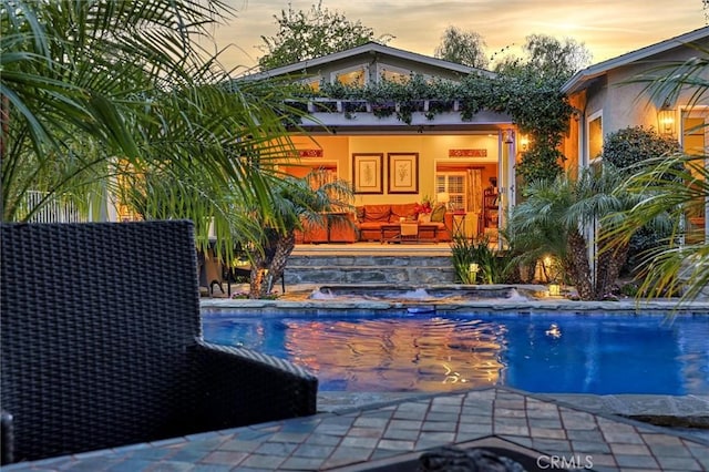 pool at dusk with an outdoor pool and a patio