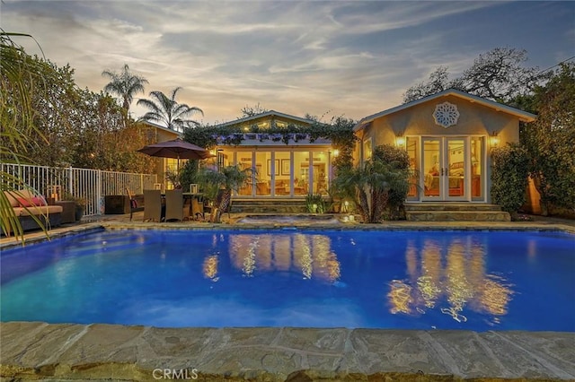 pool at dusk featuring fence, a fenced in pool, and french doors