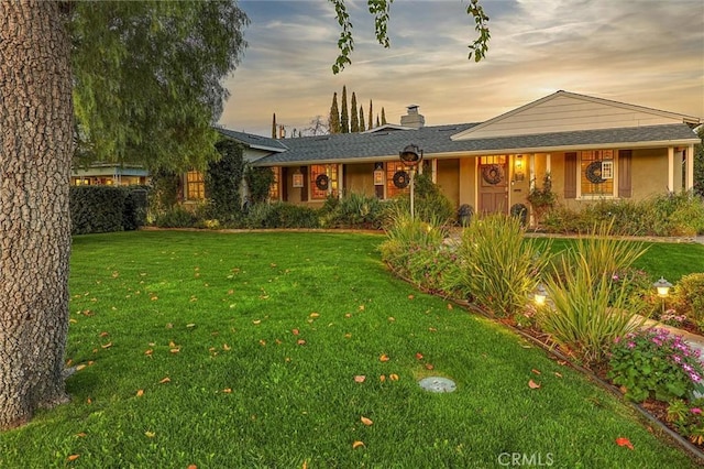 single story home with a chimney, a lawn, and stucco siding