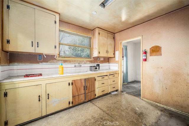 kitchen featuring tile counters, a sink, decorative backsplash, and light floors