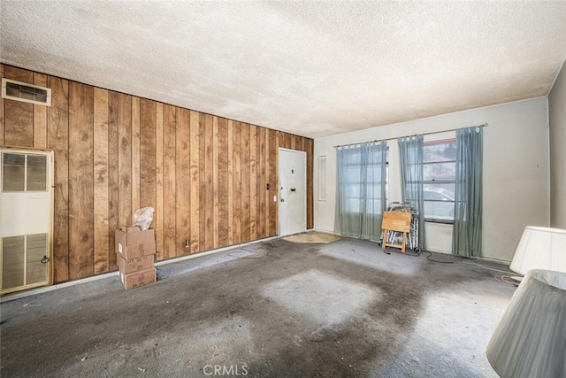 spare room with a heating unit, wooden walls, visible vents, and a textured ceiling