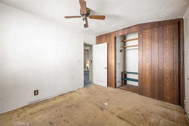 unfurnished bedroom featuring ceiling fan, a closet, and wooden walls