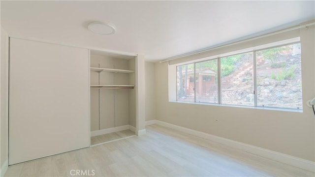 unfurnished bedroom featuring a closet, baseboards, multiple windows, and wood finished floors