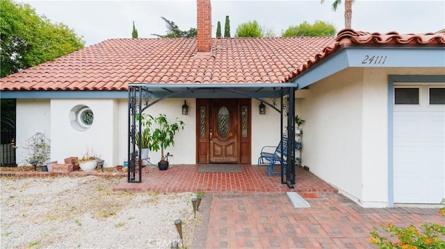 property entrance with a tile roof, stucco siding, a garage, and a chimney