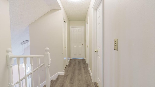 hall featuring an upstairs landing, a textured ceiling, baseboards, and light wood finished floors