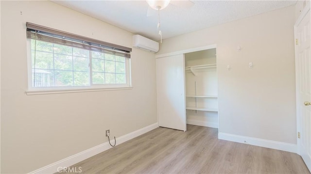 unfurnished bedroom featuring a wall mounted AC, wood finished floors, baseboards, and a closet