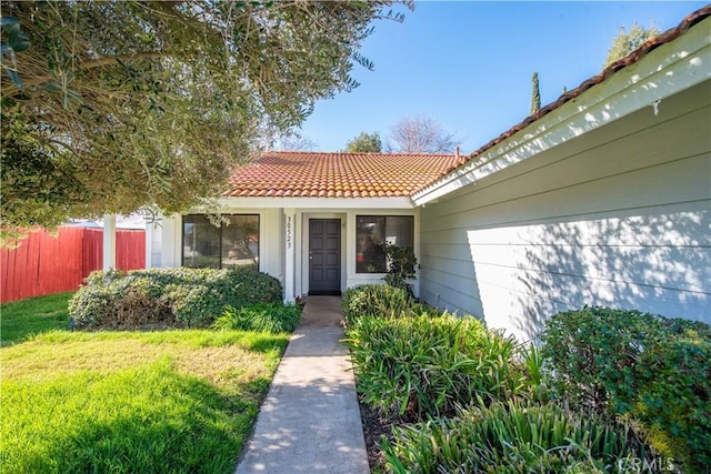 view of exterior entry with a yard, fence, and a tiled roof