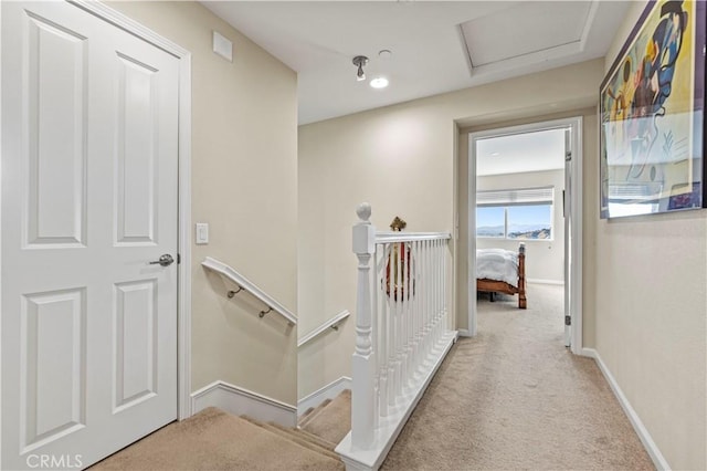 corridor with carpet, attic access, baseboards, and an upstairs landing