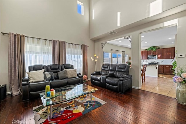 living room featuring a high ceiling, dark wood-style flooring, visible vents, and baseboards