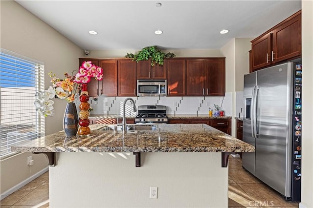 kitchen featuring light tile patterned floors, appliances with stainless steel finishes, backsplash, a breakfast bar area, and a sink