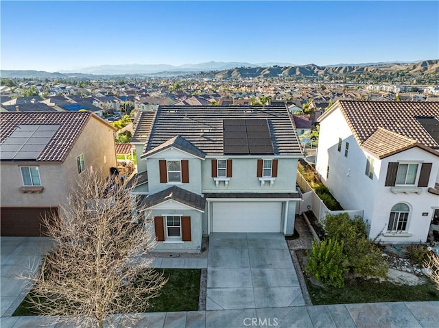 view of front facade featuring an attached garage, a mountain view, concrete driveway, a residential view, and roof mounted solar panels