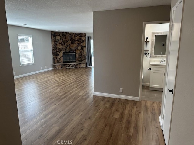 unfurnished living room featuring plenty of natural light, baseboards, wood finished floors, and a stone fireplace