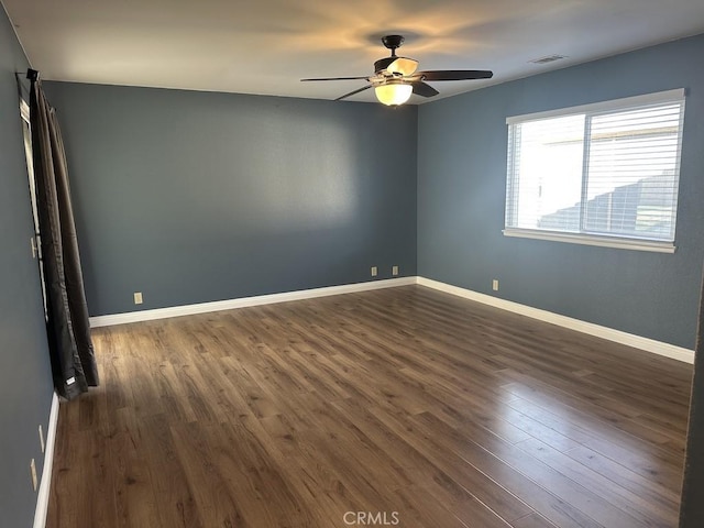 spare room with dark wood-style flooring, visible vents, ceiling fan, and baseboards