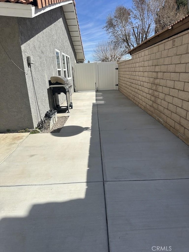 view of home's exterior featuring a patio, fence, concrete driveway, a gate, and stucco siding