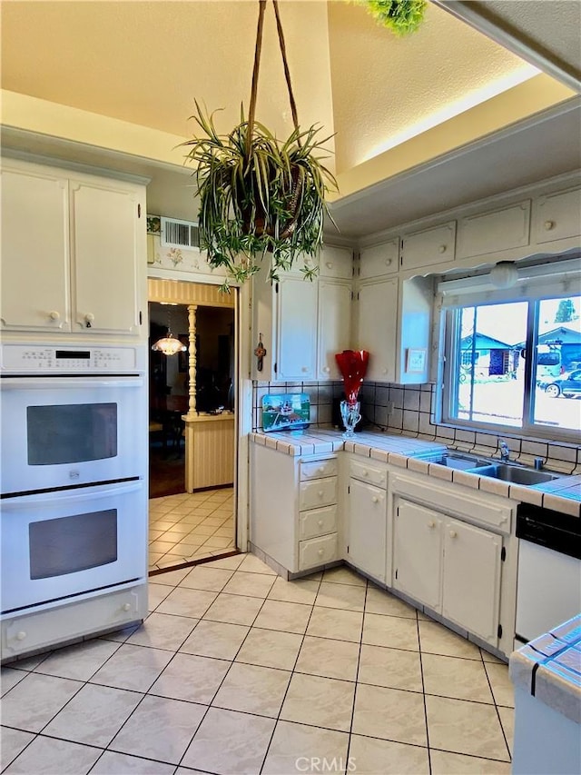 kitchen with tile countertops, white appliances, light tile patterned flooring, and white cabinetry