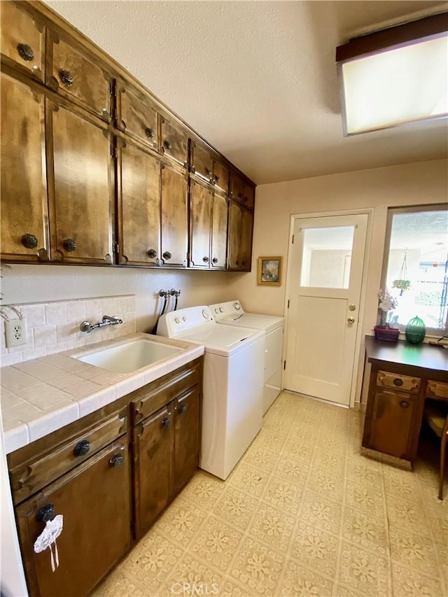 clothes washing area featuring washer and clothes dryer, light floors, cabinet space, a sink, and a textured ceiling