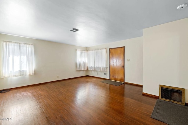 empty room with dark wood finished floors, heating unit, visible vents, a glass covered fireplace, and baseboards