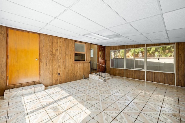 unfurnished room with a sunroom, a paneled ceiling, and wooden walls