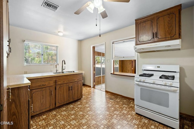 kitchen featuring white range with gas cooktop, brown cabinets, light countertops, under cabinet range hood, and a sink