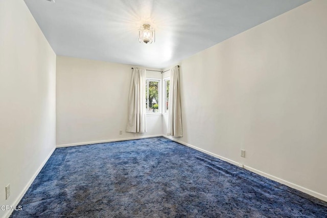 spare room featuring dark carpet and baseboards