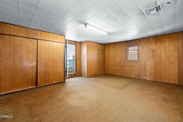 empty room featuring wooden walls, visible vents, and light carpet