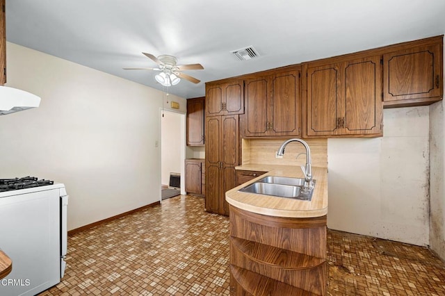 kitchen with brown cabinets, light countertops, a sink, and white gas range oven