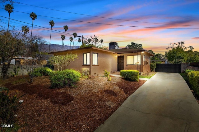 mid-century home with driveway, a chimney, fence, and stucco siding