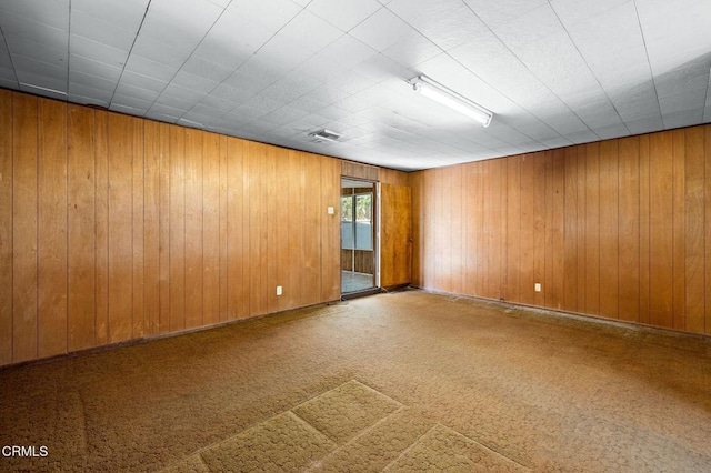 empty room featuring wooden walls, visible vents, and carpet flooring