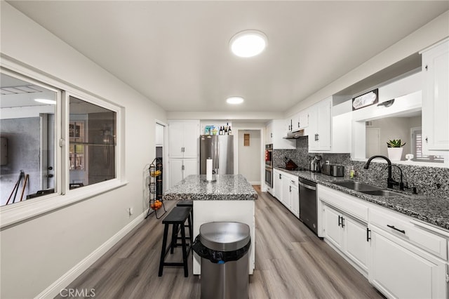 kitchen with a sink, a kitchen breakfast bar, appliances with stainless steel finishes, a center island, and dark stone countertops