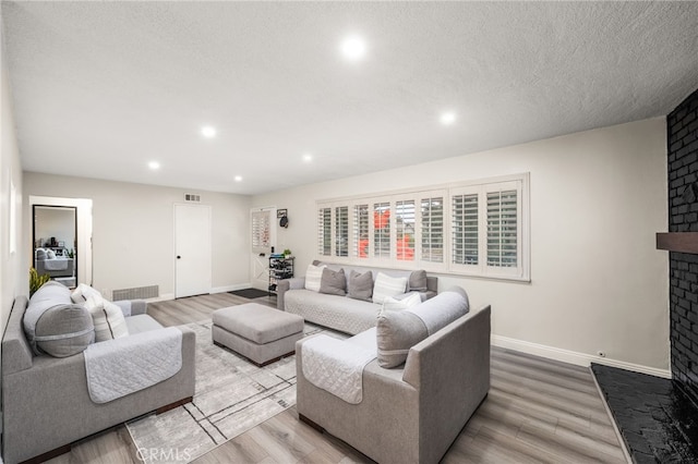 living area featuring a textured ceiling, recessed lighting, wood finished floors, baseboards, and a brick fireplace