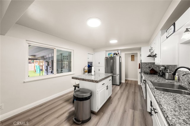 kitchen featuring light stone counters, a kitchen island, freestanding refrigerator, and white cabinetry