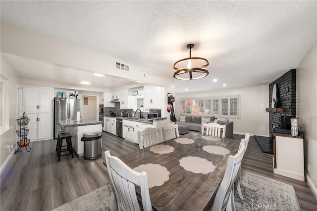 dining room featuring a fireplace, visible vents, dark wood-type flooring, a textured ceiling, and baseboards